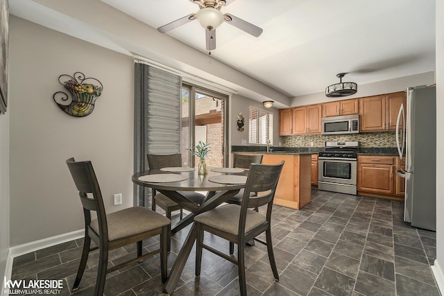 kitchen featuring stainless steel appliances, dark countertops, a ceiling fan, brown cabinetry, and backsplash