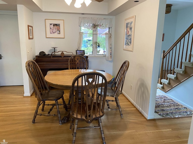 dining room featuring light wood-style flooring, stairway, baseboards, and a raised ceiling