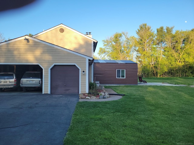 view of side of home featuring a yard, driveway, a chimney, an attached garage, and metal roof
