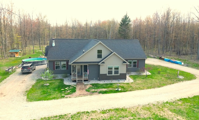 3787 Shepherd Rd, Midland, MI 48880 - view of front of house featuring a shingled roof, a forest view, covered porch, and a front lawn