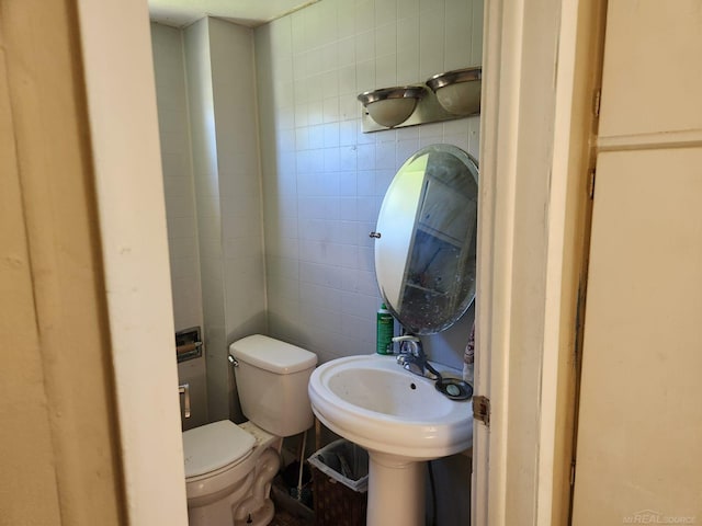 bathroom featuring toilet, tile walls, and a sink