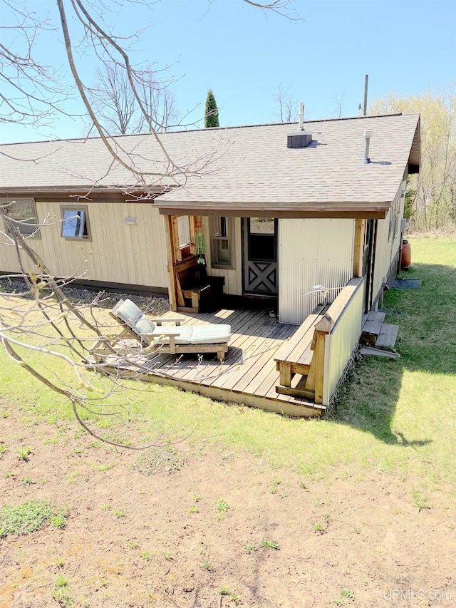 rear view of house with a deck, a shingled roof, and a yard