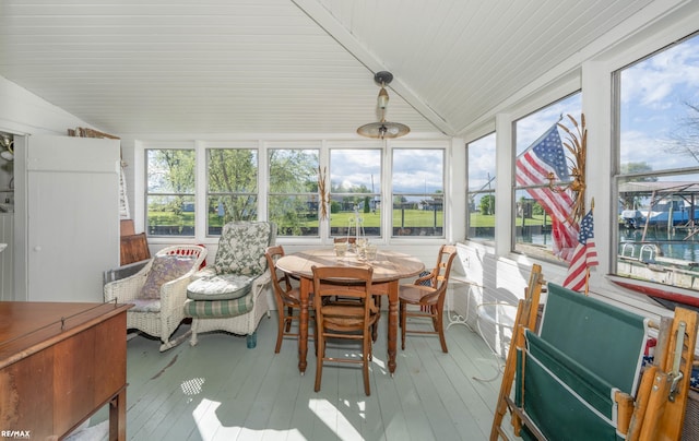 sunroom / solarium with vaulted ceiling, healthy amount of natural light, hardwood / wood-style flooring, a deck with water view, and wood ceiling
