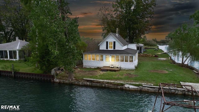 rear view of house with a sunroom, a water view, and a lawn