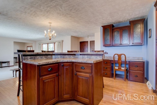 8962 Stagecoach Q.5 Ave, Gladstone, MI 49837 - kitchen featuring a breakfast bar, light wood-style flooring, a chandelier, a textured ceiling, and glass insert cabinets