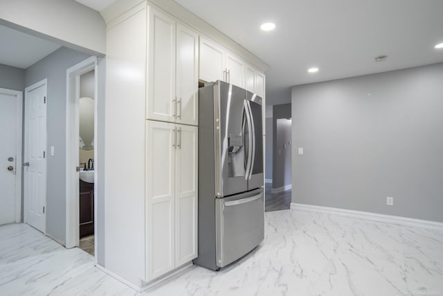 kitchen featuring stainless steel refrigerator with ice dispenser, light marble finish floors, recessed lighting, white cabinetry, and baseboards