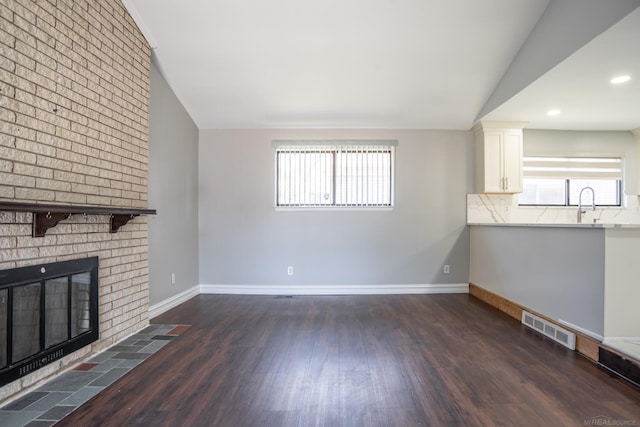 unfurnished living room featuring lofted ceiling, wood finished floors, baseboards, a fireplace, and recessed lighting