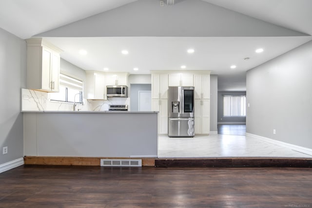 kitchen featuring appliances with stainless steel finishes, vaulted ceiling, a peninsula, a sink, and baseboards