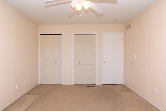 unfurnished bedroom with multiple closets, carpet, and a ceiling fan