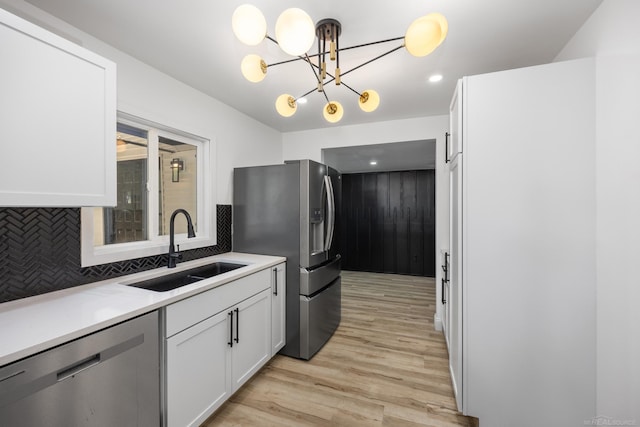 kitchen featuring stainless steel appliances, a sink, light wood-style floors, white cabinetry, and a chandelier