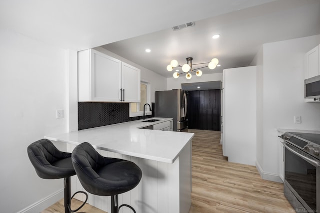 kitchen with stainless steel appliances, light wood-style flooring, a kitchen bar, white cabinets, and a peninsula