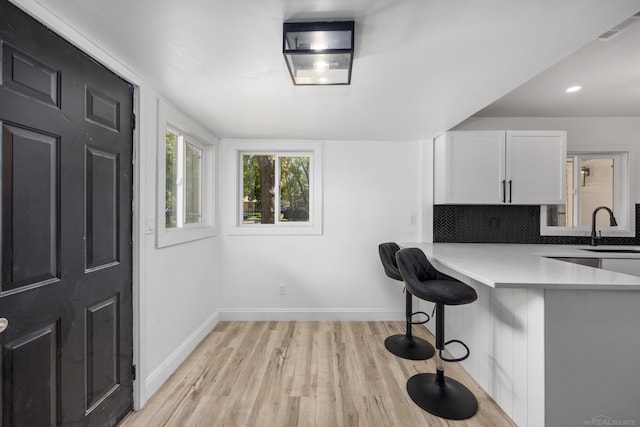 kitchen featuring light wood-style floors, light countertops, baseboards, a breakfast bar, and white cabinetry