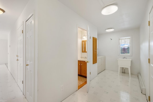 corridor with washing machine and dryer, a baseboard heating unit, a sink, and light flooring