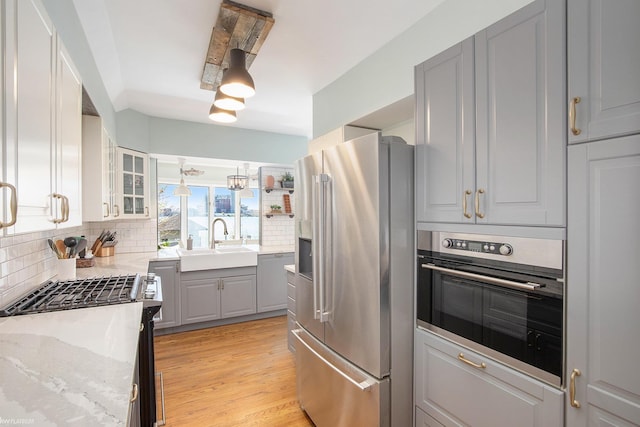 2758 Military St, Port Huron, MI 48060 - kitchen with appliances with stainless steel finishes, a sink, gray cabinetry, tasteful backsplash, and glass insert cabinets