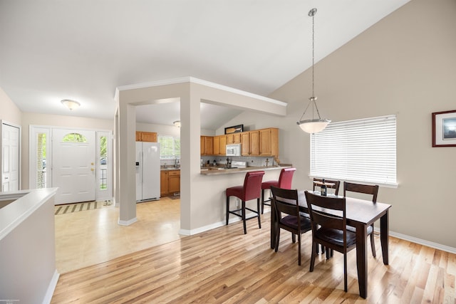 dining space featuring light wood-style floors, baseboards, and vaulted ceiling