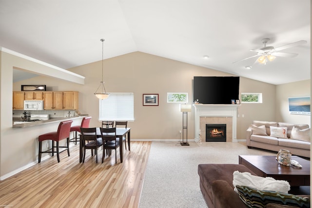 living room featuring lofted ceiling, a tiled fireplace, ceiling fan, baseboards, and light wood-style floors