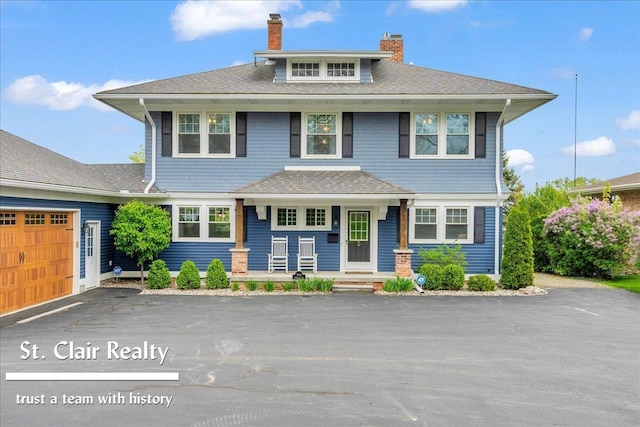 traditional style home with a porch, a chimney, driveway, a garage, and roof with shingles