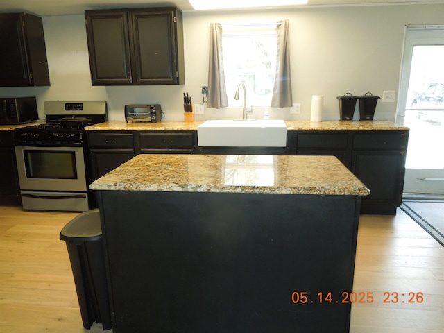 1582 Oakwood St, Gladwin, MI 48624 - kitchen featuring appliances with stainless steel finishes, a sink, light wood-style flooring, dark cabinetry, and a kitchen island