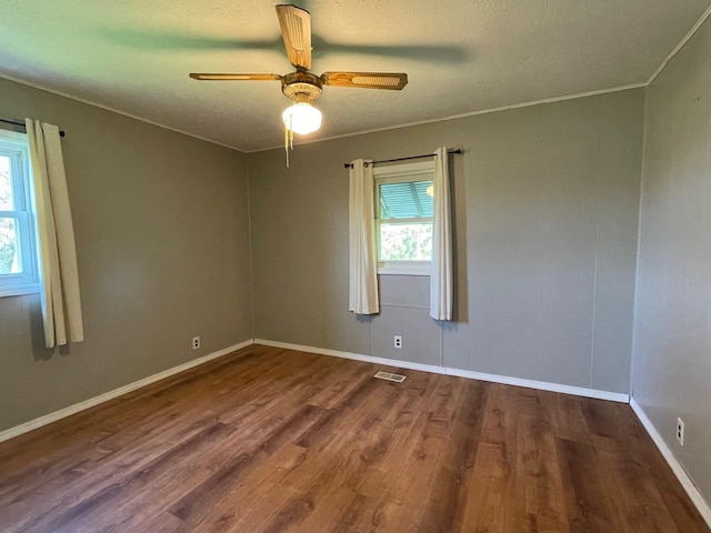 spare room featuring wood finished floors, ornamental molding, ceiling fan, baseboards, and a textured ceiling