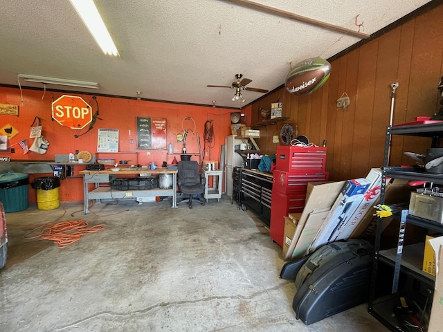 garage featuring a workshop area, a ceiling fan, and wood walls