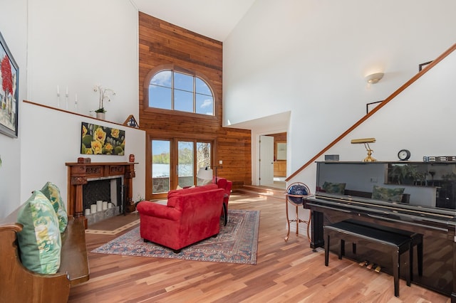 living room with high vaulted ceiling, wooden walls, plenty of natural light, wood finished floors, and a fireplace