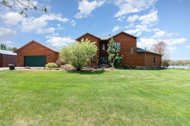 view of grassy yard with a garage, a water view, and an outbuilding
