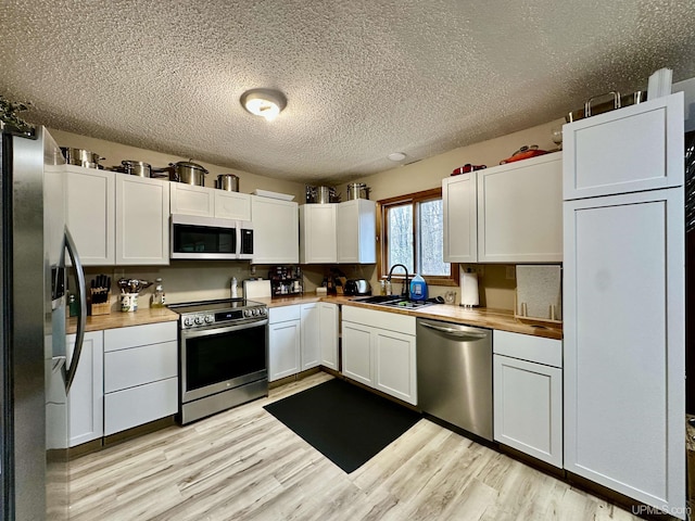 39 Stonegate Hts, Marquette, MI 49855 - kitchen with stainless steel appliances, a sink, light wood finished floors, a textured ceiling, and white cabinets