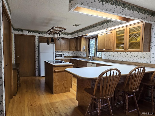 1604 Mildred Ave, Marquette, MI 49855 - kitchen featuring wallpapered walls, white appliances, a kitchen island, light wood finished floors, and a textured ceiling