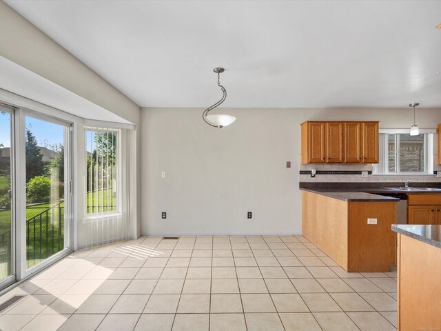 55374 Raspberry Dr, Macomb Twp, MI 48042 - kitchen featuring dark countertops, brown cabinetry, tasteful backsplash, hanging light fixtures, and light tile patterned floors