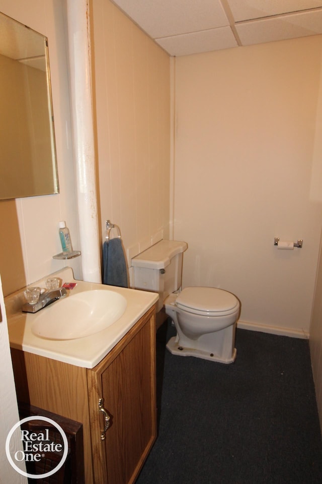 half bathroom with vanity, toilet, and a drop ceiling