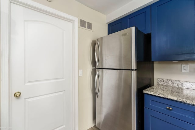 kitchen with freestanding refrigerator, blue cabinets, and light stone countertops