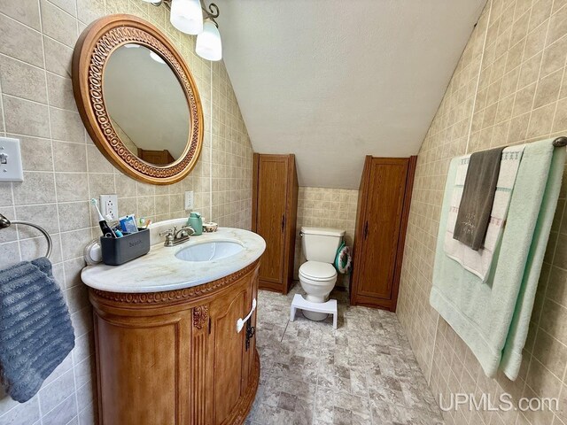 624 S 16th St, Escanaba, MI 49829 - bathroom with tile walls, vaulted ceiling, toilet, vanity, and stone finish flooring