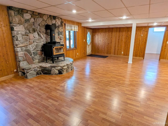 1002 Allouez Rd, Marquette, MI 49855 - unfurnished living room featuring baseboards, wood finished floors, a wood stove, a paneled ceiling, and healthy amount of natural light
