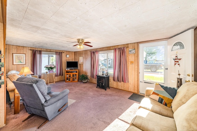 125 Wickham Ave, Houghton Lake, MI 48629 - living area featuring wood walls, carpet flooring, a wood stove, and a ceiling fan