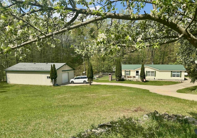 view of green lawn featuring driveway, an outdoor structure, and a garage