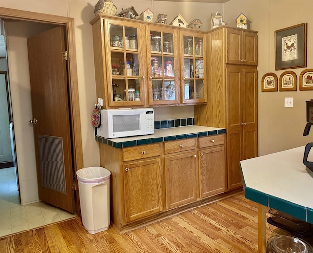 kitchen featuring white microwave, glass insert cabinets, light wood-type flooring, and brown cabinets
