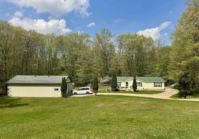 view of grassy yard featuring driveway and a wooded view