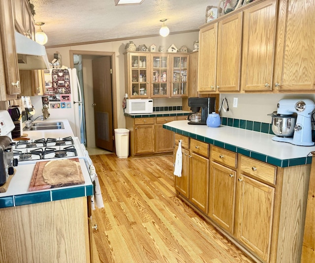 kitchen featuring white appliances, range hood, light wood finished floors, a sink, and a textured ceiling