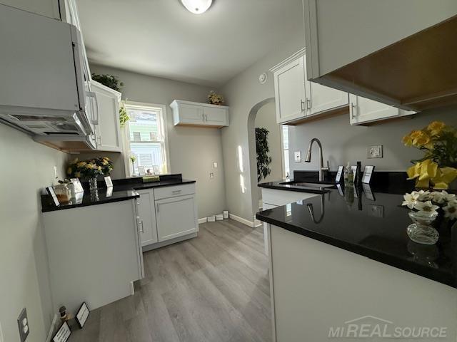 1416 Kearney St, Port Huron, MI 48060 - kitchen with dark countertops, light wood finished floors, arched walkways, white cabinets, and a sink
