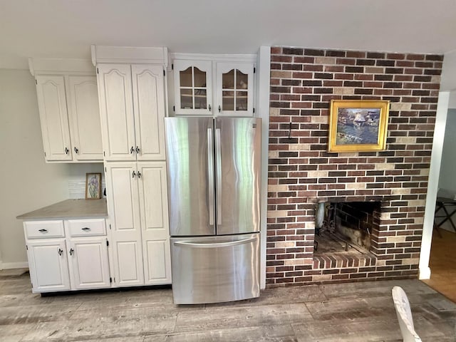 555 W Saxton Rd, Sanford, MI 48657 - kitchen featuring freestanding refrigerator, light wood finished floors, white cabinetry, a brick fireplace, and light countertops