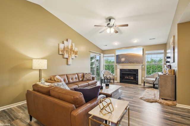 living room with ceiling fan, lofted ceiling, plenty of natural light, a glass covered fireplace, and wood finished floors