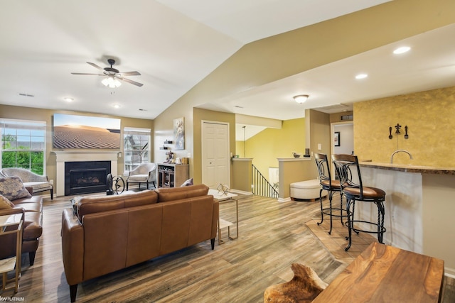 living area featuring ceiling fan, lofted ceiling, a fireplace, wood finished floors, and baseboards