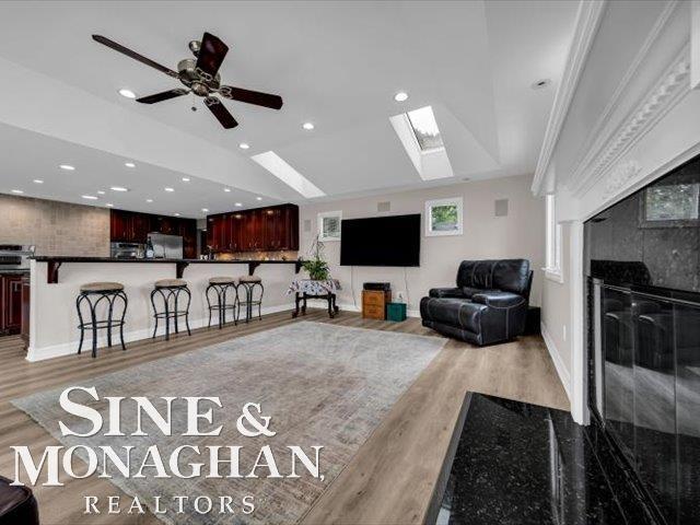 living area featuring light wood-style floors, a skylight, a tile fireplace, recessed lighting, and a ceiling fan