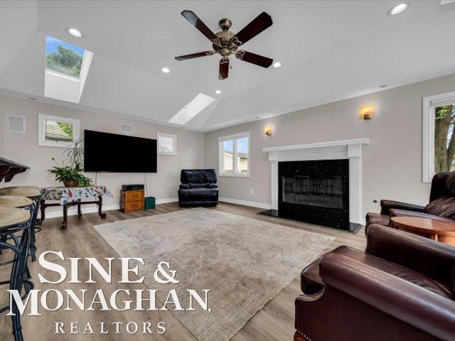 living area with a skylight, wood finished floors, recessed lighting, a ceiling fan, and a high end fireplace