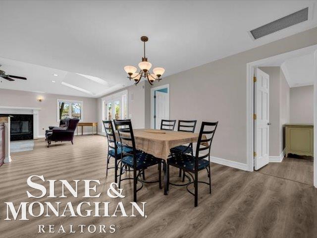 dining space with wood finished floors, a chandelier, a fireplace, and baseboards
