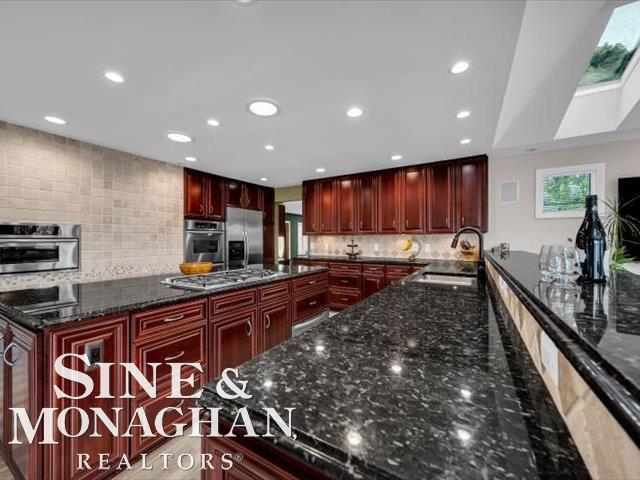 kitchen featuring stainless steel appliances, a sink, reddish brown cabinets, decorative backsplash, and recessed lighting