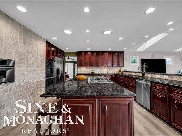 kitchen featuring reddish brown cabinets, appliances with stainless steel finishes, dark stone countertops, light wood-style floors, and recessed lighting