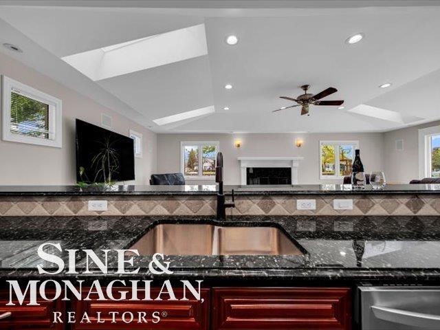 kitchen with a sink, dark brown cabinets, dark stone countertops, recessed lighting, and ceiling fan