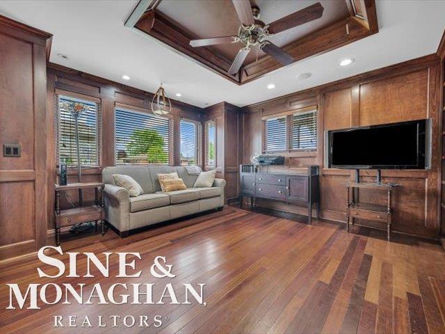 living area with ceiling fan, healthy amount of natural light, dark wood-type flooring, wooden walls, and recessed lighting