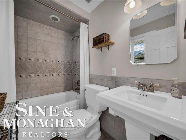 full bath with shower / tub combo, toilet, tile walls, and a sink
